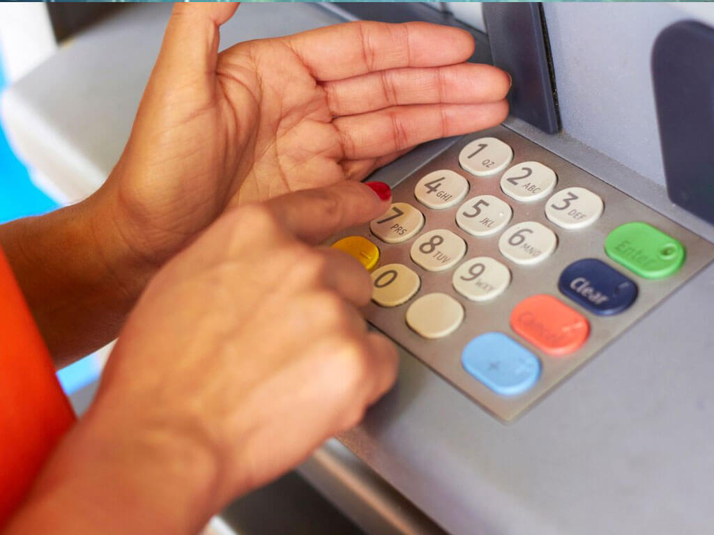 Someone using hand to hide while typing pin code on ATM