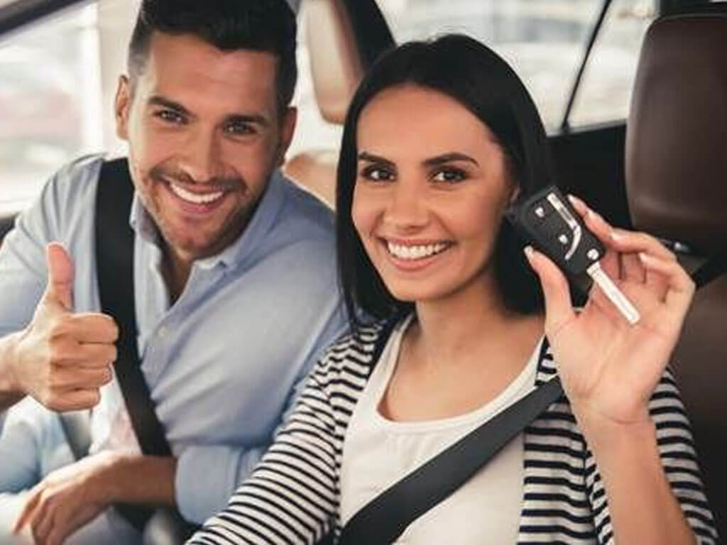 A happy couple inside a car - woman holding a car key