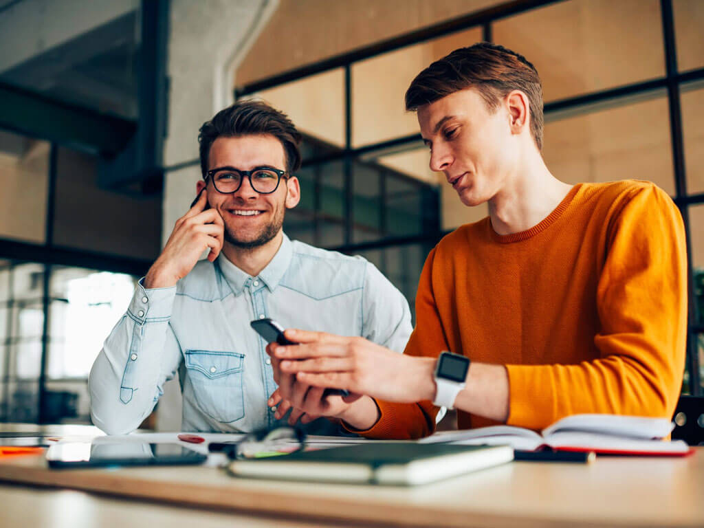 Two man smiling and using their smartphones
