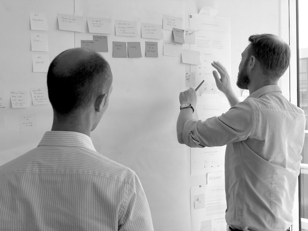 Two man looking at a white board with lots of notes
